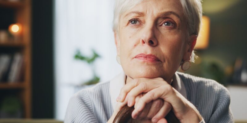 Woman with dementia sitting alone and looking out thoughtfully.