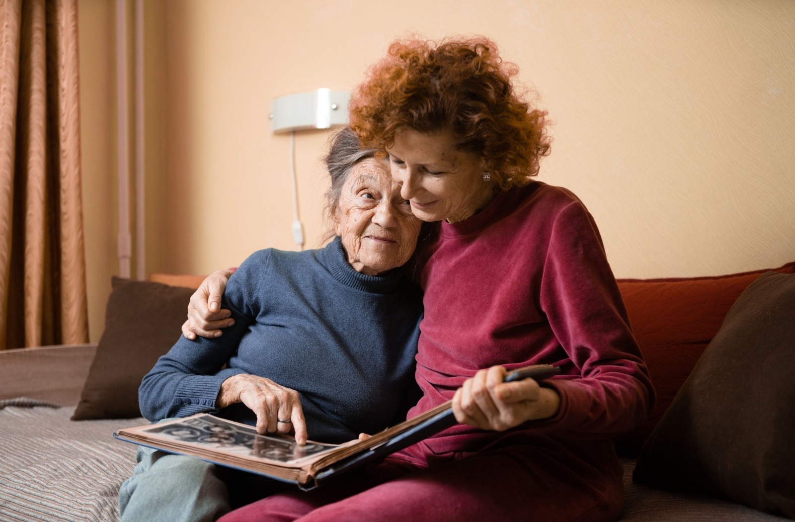 An older adult and their senior parent reminisce as they flip through a family photo album together.
