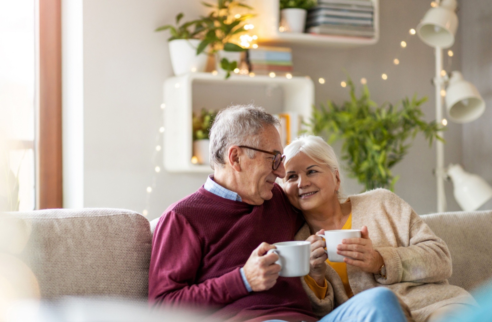 A smiling senior couple relax with a cup of coffee while sitting on a sofa in their senior living apartment.
