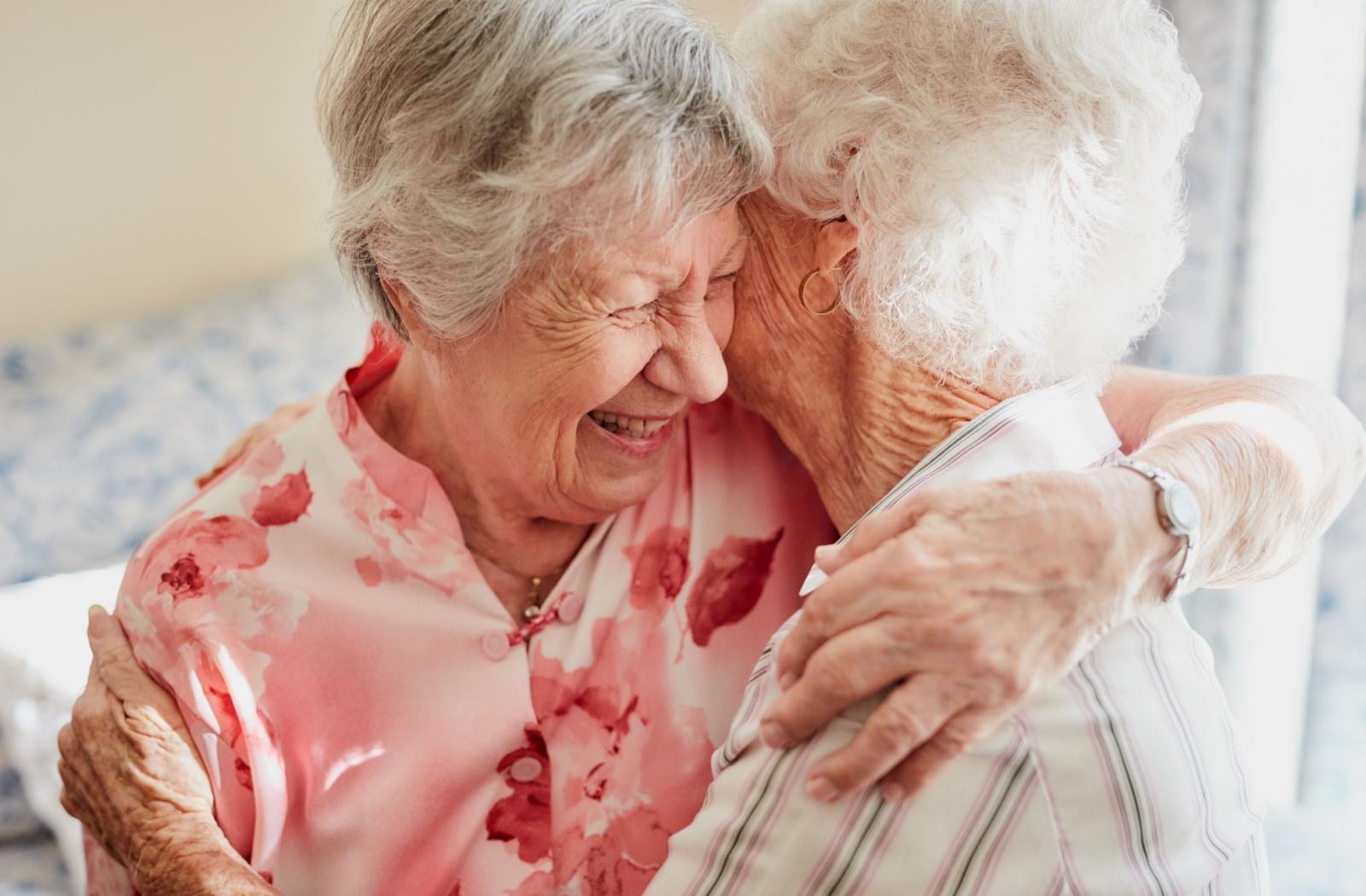 Two senior friends smile as they share an embrace.